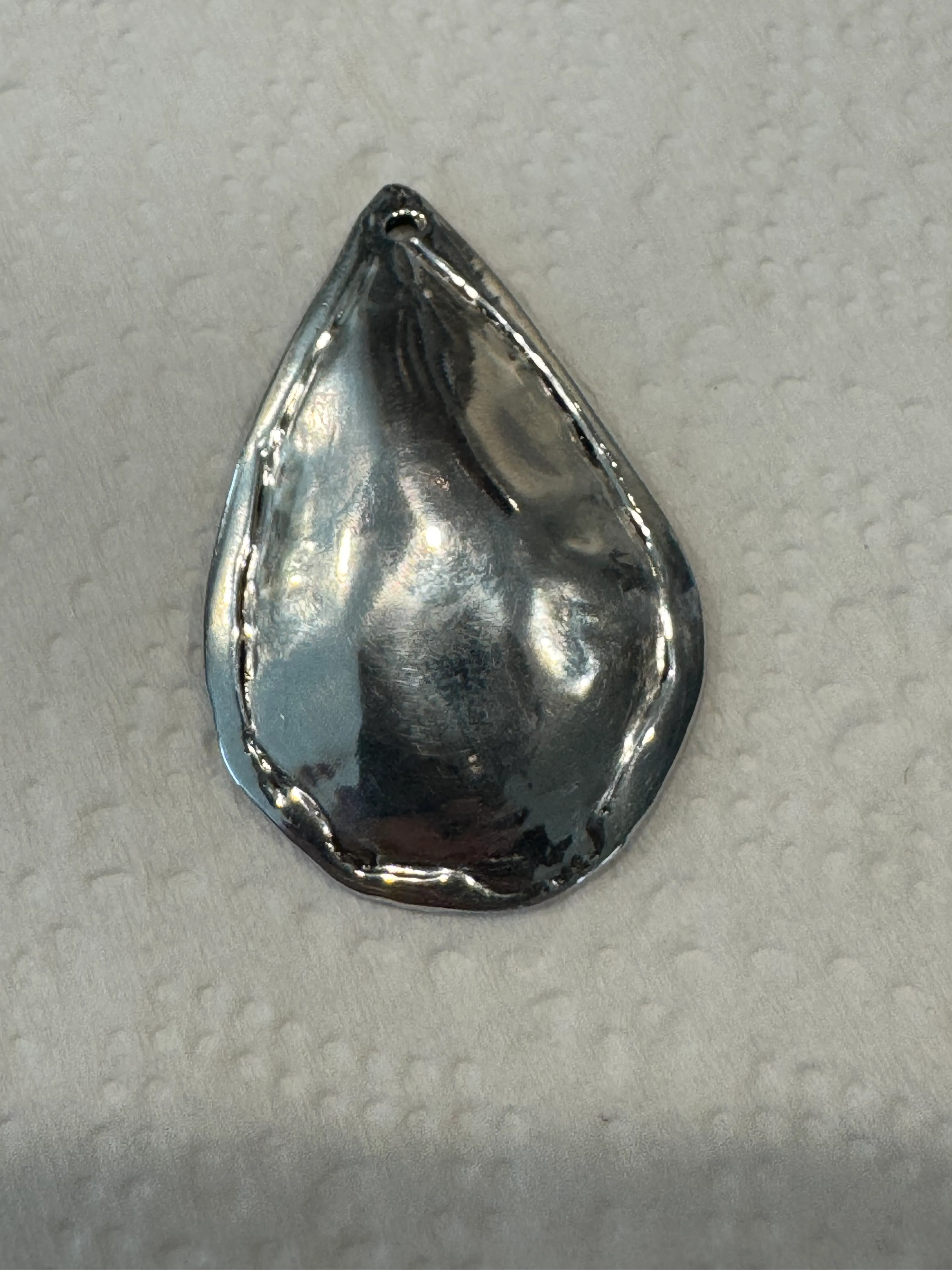 The back of the pendant: a domed, polished silver surface with a rippled wrapped rim running around the edge and a dark scorch mark near the bottom.