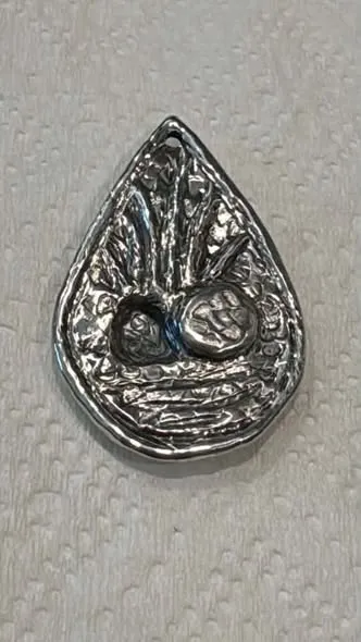 A small teardrop-shaped silver pendant, darkened and polished back, showing a raised disc beside a sunken arched opening with rays fanning upward.
